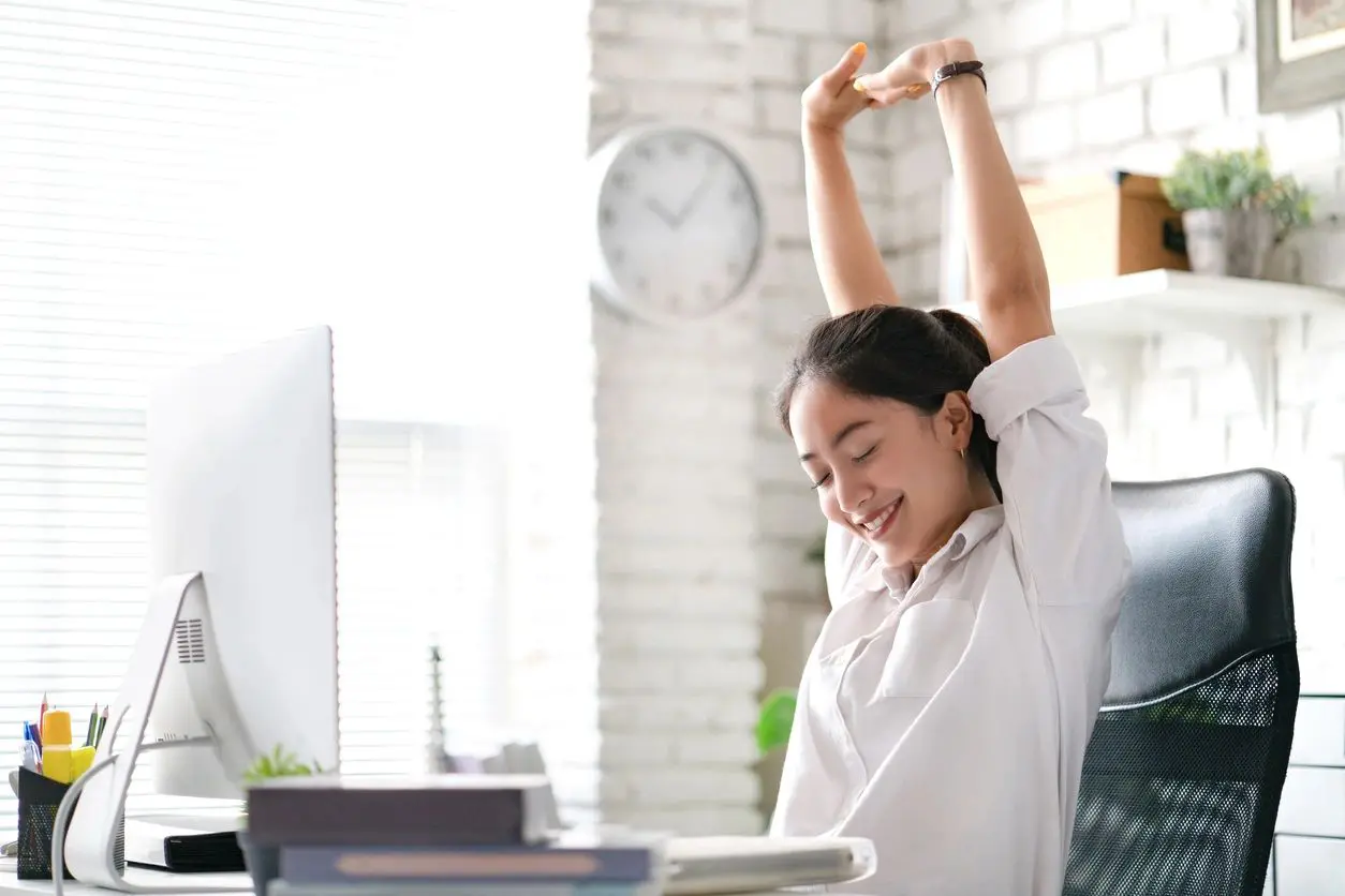 Happy and content female office worker stretching at her desk